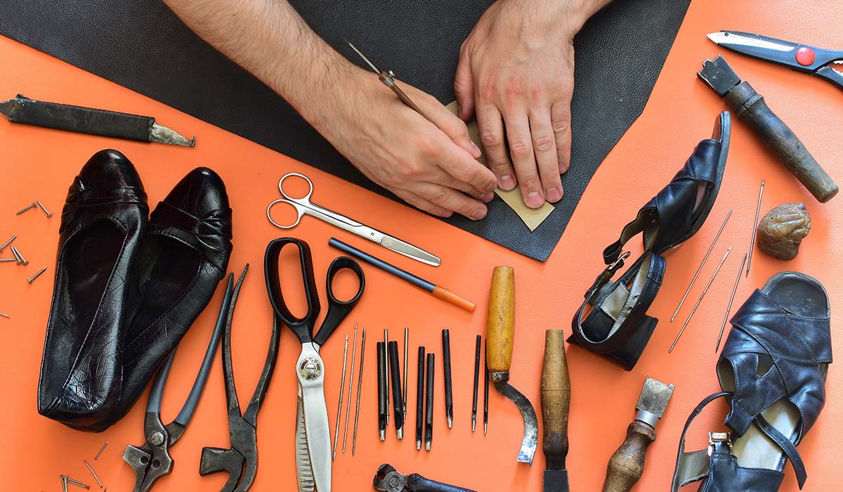 Pengrajin sepatu sedang membuat pola kulit sepatu wanita dengan alat tradisional di bengkel sepatu.
