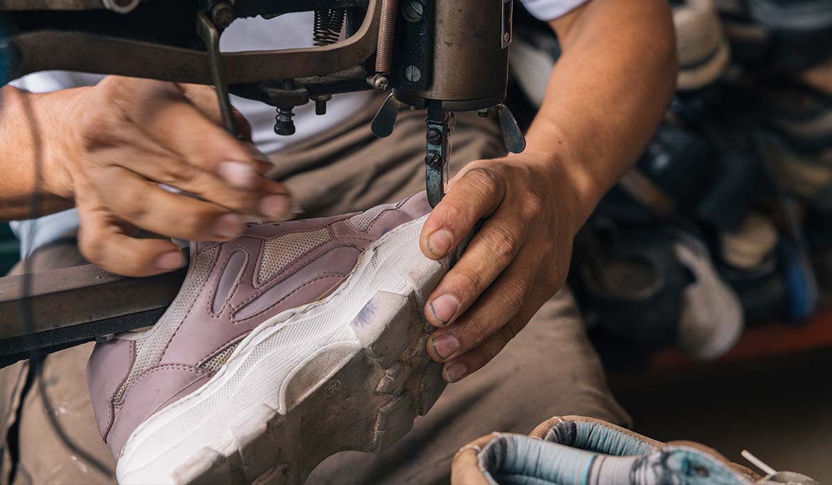 Pengrajin menggunakan mesin jahit untuk menjahit sepatu olahraga di pabrik