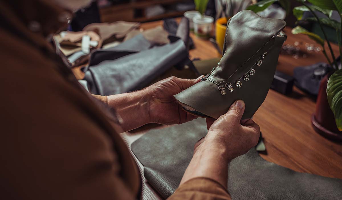 Pengrajin sepatu sedang memegang dan memeriksa bagian upper sepatu berbahan kulit dalam proses pembuatan sepatu handmade