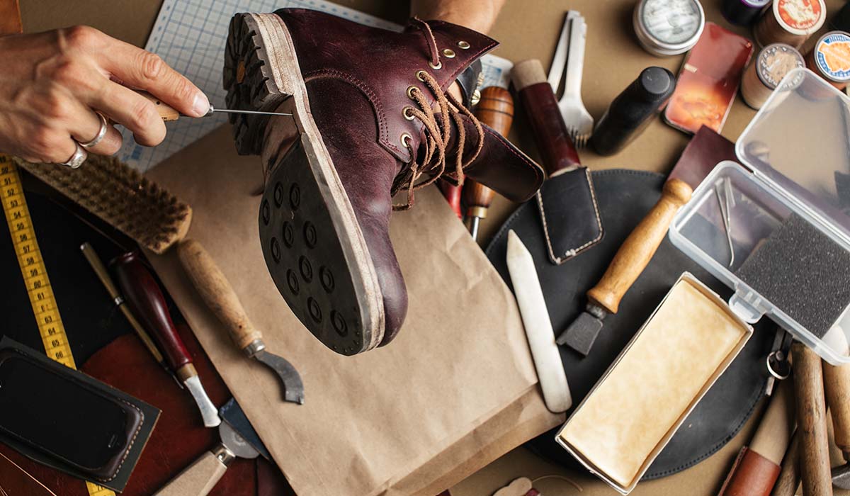 Pengrajin sepatu sedang membuat sepatu boots kulit handmade dengan alat tradisional di bengkel sepatu lokal.