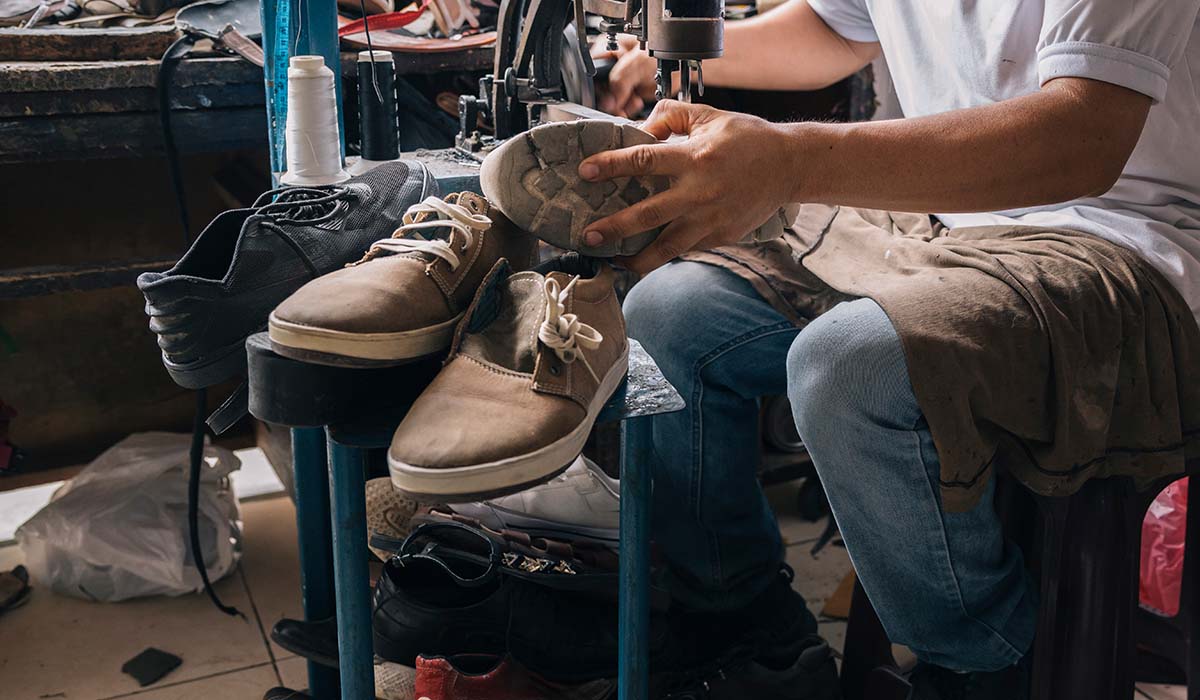 Pengrajin sedang menjahit sol sepatu olahraga di bengkel sepatu