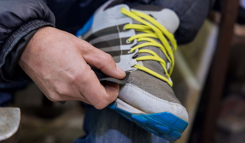 Perajin sepatu olahraga sedang memperbaiki dan merapikan sepatu dalam proses produksi