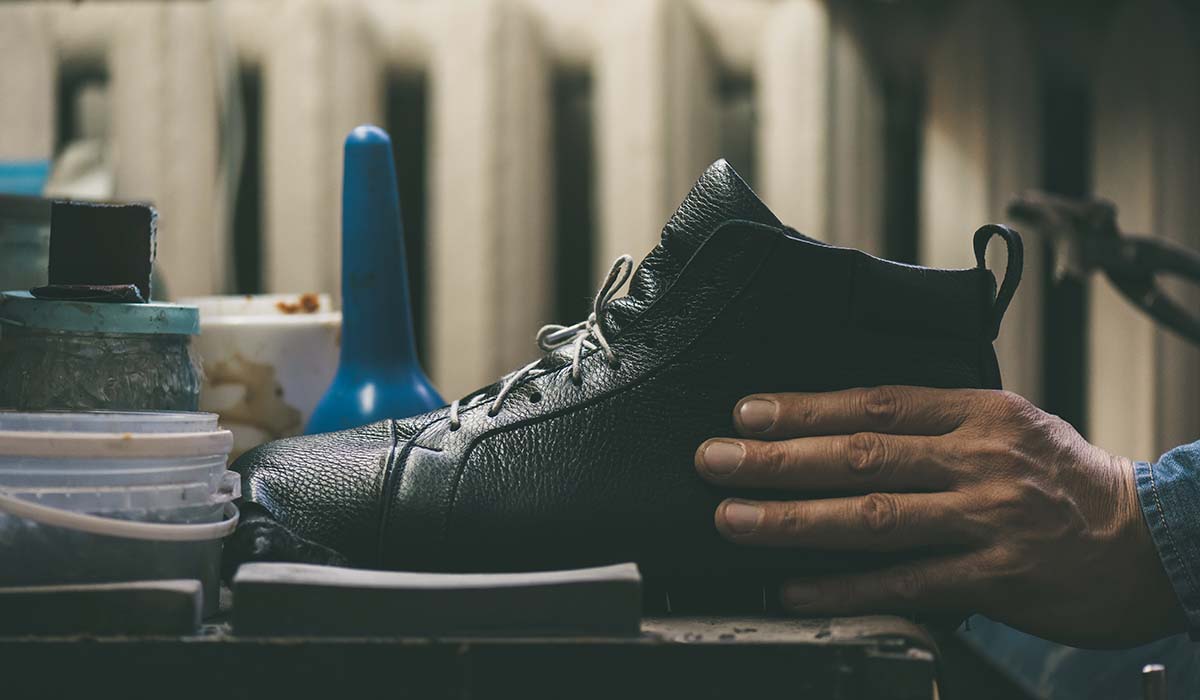 Pengrajin merakit dan membentuk sepatu olahraga secara manual