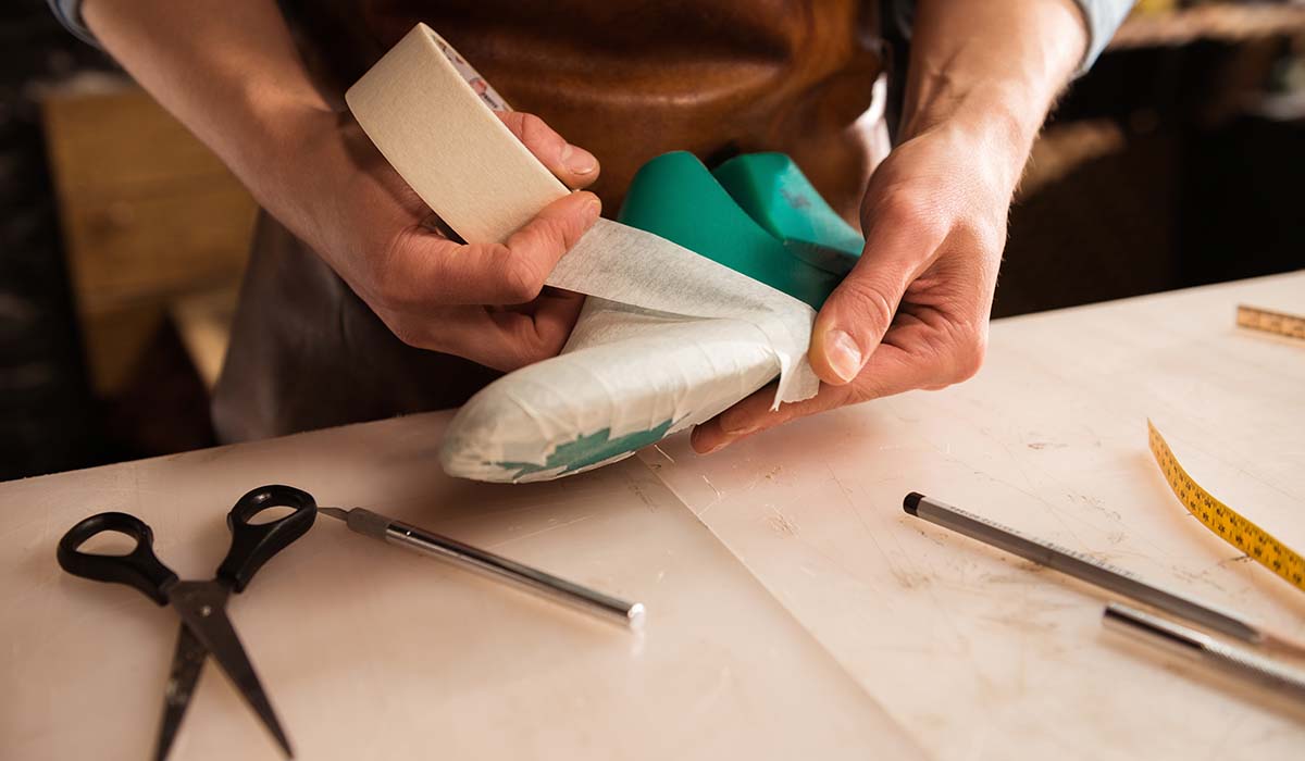 Pengrajin menyiapkan pola sepatu pada cetakan kaki (shoe last) dalam tahap desain