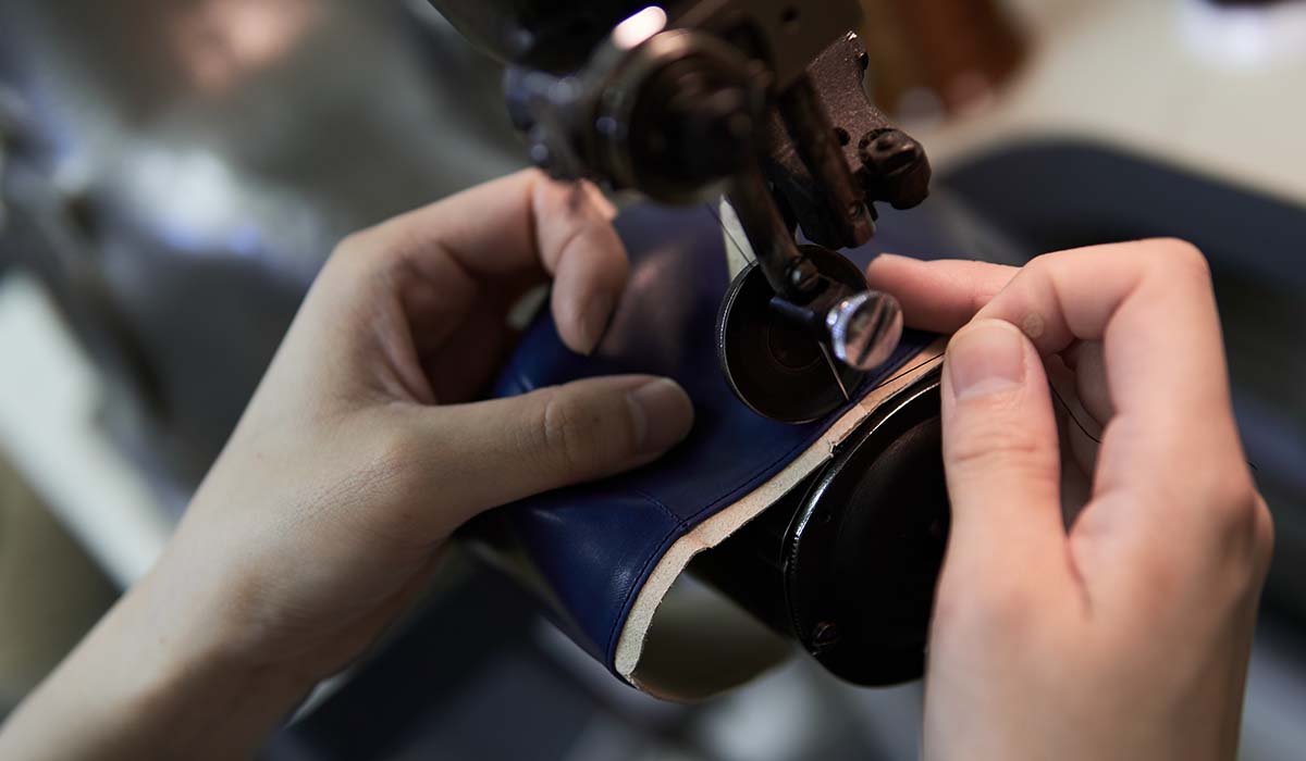 Tangan pengrajin sedang menjahit bahan kulit untuk sepatu olahraga