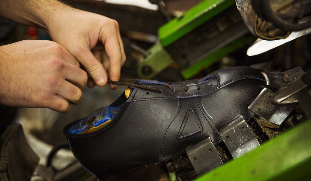 Pengrajin sepatu sedang memasang tali pada sepatu kulit handmade dalam proses finishing pembuatan sepatu