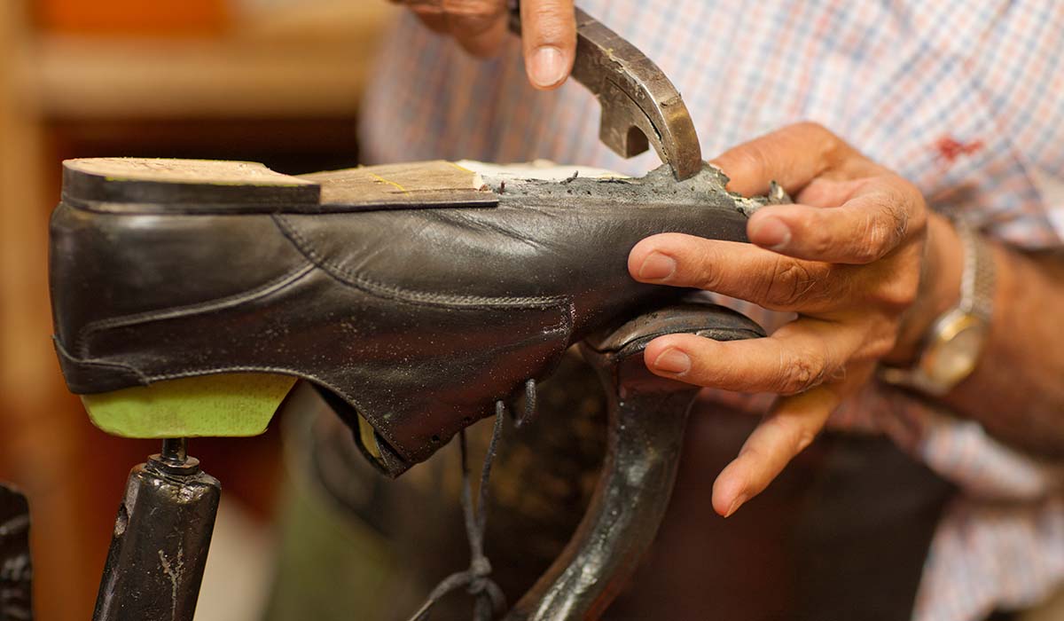 Pengrajin sepatu sedang memaku bagian sol sepatu kulit dalam proses pembuatan sepatu di vendor sepatu profesional.